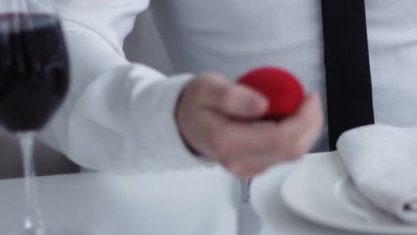 Nahaufnahme Mann hält Box mit Ring macht seiner Freundin einen Heiratsantrag, Restaurant - Filmmaterial, Video