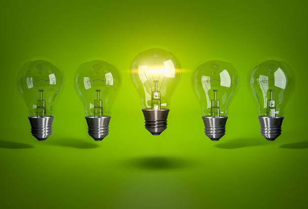 Glowing bulb in row of light bulb on green background - Photo, Image