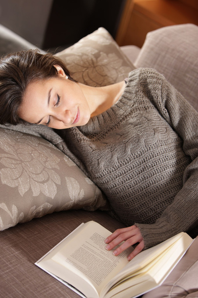 Woman lying on couch with book - 写真・画像