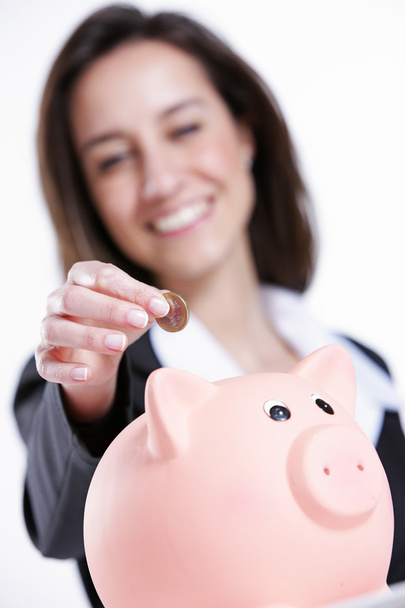 Close-up of young woman putting coin into a piggy bank - Foto, afbeelding