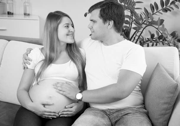 Retrato en blanco y negro de una feliz pareja embarazada sentada en el suelo
 - Foto, Imagen