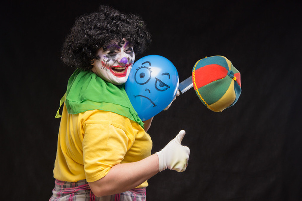 Angry ugly clown wants to kill a balloon in the cap - Photo, Image