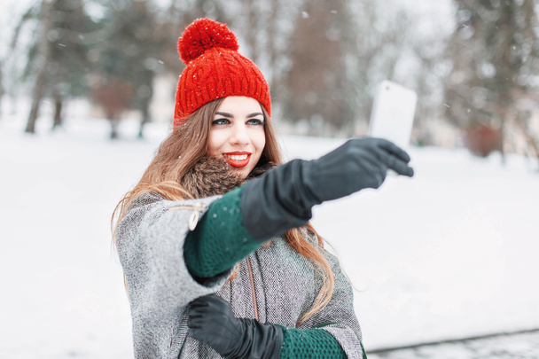 Selfie time. Joyful young women making selfie by her smart phone. Winter snowy day. Outdoors. - Zdjęcie, obraz