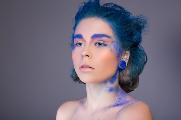 wunderschöne junge Frau mit blauen Haaren, Ohrringen, Make-up auf grauem Hintergrund im Studio - Foto, Bild