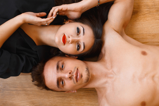 Young couple lying on the wooden floor and looking up. top view - Foto, Imagem
