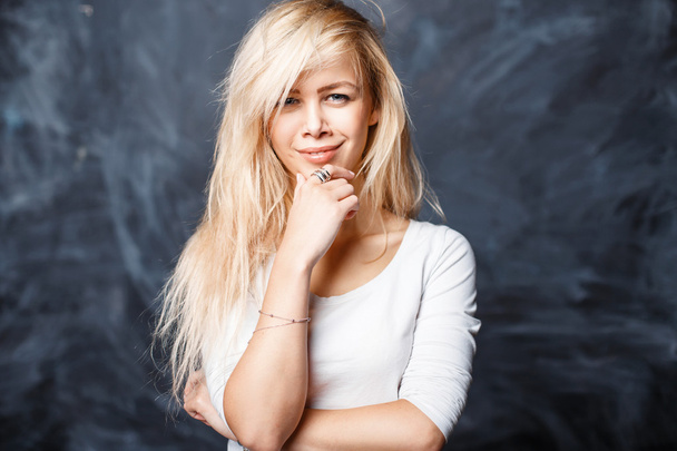 schöne junge blonde Mädchen in einem weißen Hemd lächelt vor einem dunklen Hintergrund mit Flecken - Foto, Bild