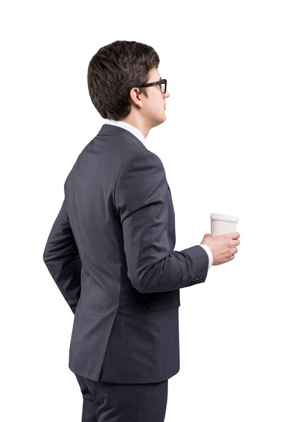 A young man in a black suit holding a paper cup. White background. Concept of coffee break. Isolated - Фото, изображение