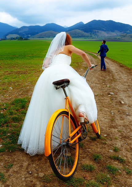 bride on orange retro bike is chasing after a groom in blue wedding suit with a beer bottle. wedding concept. - Foto, immagini