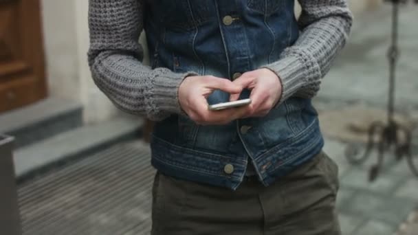 Homem atraente na casa dos 20 usando dispositivo móvel digitando no celular e criando uma mensagem. Jovem fazendo uma chamada e sorrindo ao ar livre
. - Filmagem, Vídeo