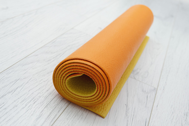 φωτεινό πορτοκαλί γιόγκα χαλάκι για ένα ελαφρύ γκρι φύλλο πλαστικού, σε εσωτερικούς χώρους - Φωτογραφία, εικόνα