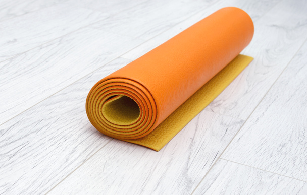 helder oranje yoga mat op een licht grijs laminaat, binnenshuis - Foto, afbeelding