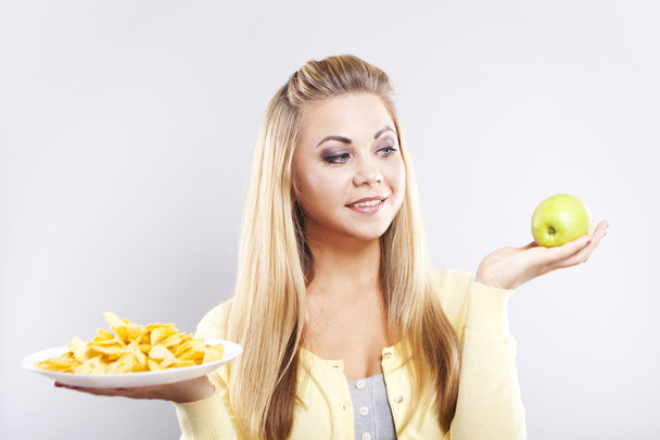 Meisje kiest tussen een appel en aardappel chips. Blonde denken wat te eten. - Foto, afbeelding