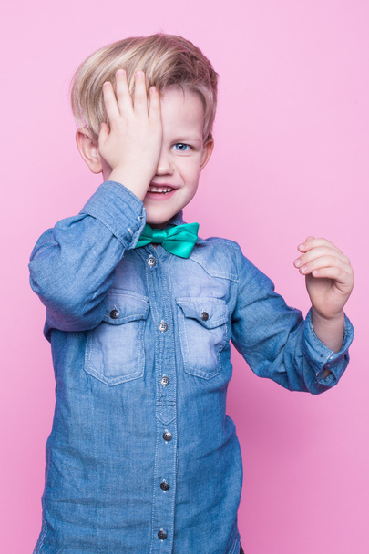 Young beautiful boy with blue shirt and butterfly tie. Studio portrait over pink background - Foto, immagini