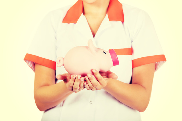 Young female doctor or nurse holding a piggybank - Fotó, kép
