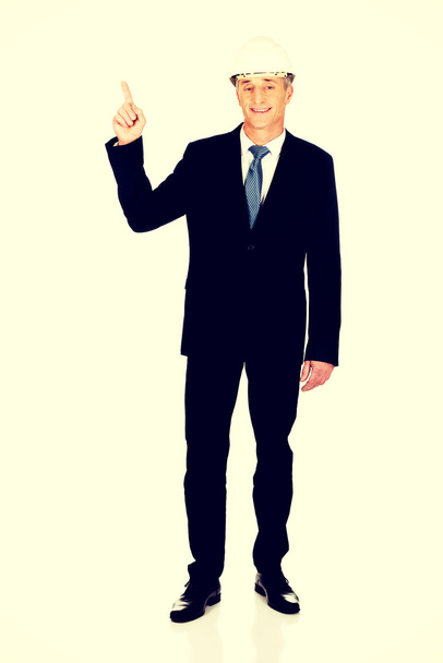 Smiling businessman with hard hat pointing up - Fotó, kép