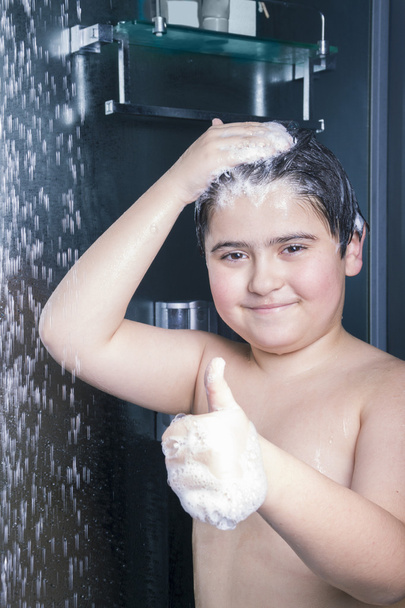 lächelnder Junge wäscht sich unter der Dusche den Kopf und zeigt Daumen - Foto, Bild
