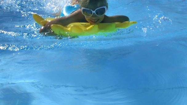 Kind dragen zonnebril drijvend op opblaasbare ring zijn zwemmen in zwembad. - Video