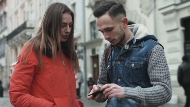 Νεαρό ζευγάρι χρησιμοποιώντας κινητή συσκευή σε εξωτερικούς χώρους στο κέντρο της πόλης του Ευρωπαϊκού. - Πλάνα, βίντεο