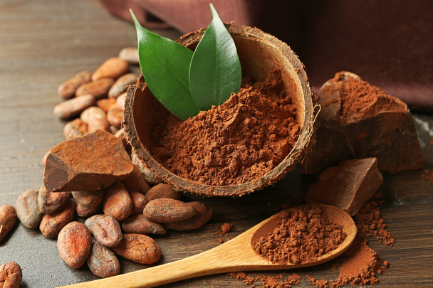Bowl with aromatic cocoa powder and green leaf on wooden background, close up - 写真・画像