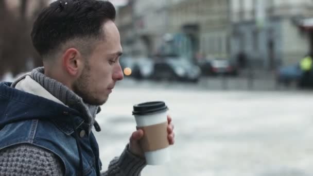 Mladý muž se pití kávy s sebou venku a čeká na někoho. Atraktivní muž upíjel kávu v centru města a zároveň se těší na svého přítele. - Záběry, video