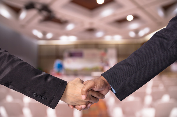 Рукопожатие между бизнесменом и предпринимательницей о размытом фото подготовки митинга в ярком конференц-зале
 - Фото, изображение