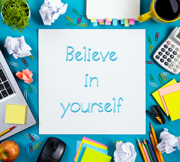 Believe in yourself. Office table desk with supplies, white blank note pad, cup, pen, pc, crumpled paper, flower on wooden background. Top view - Photo, Image