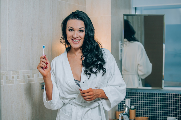 Portrait of attractive woman brushing teeth in bathroom  a white coat. healthy teeth. - 写真・画像