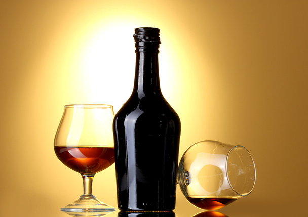 Glasses of brandy and bottle on yellow background - Foto, Bild