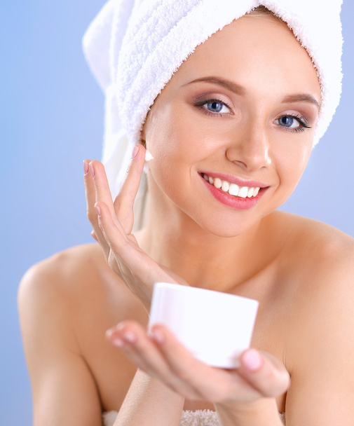 Mooie jonge vrouw, een crème op haar gezicht geïsoleerd op grijze achtergrond toe te passen - Foto, afbeelding