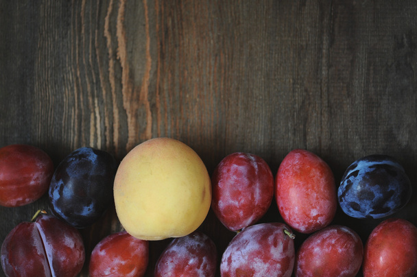 Peaches and plums on dark wooden table. - Foto, afbeelding