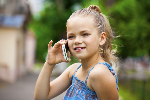 Little girl talking on cell phone against green of Park in summe - Фото, изображение