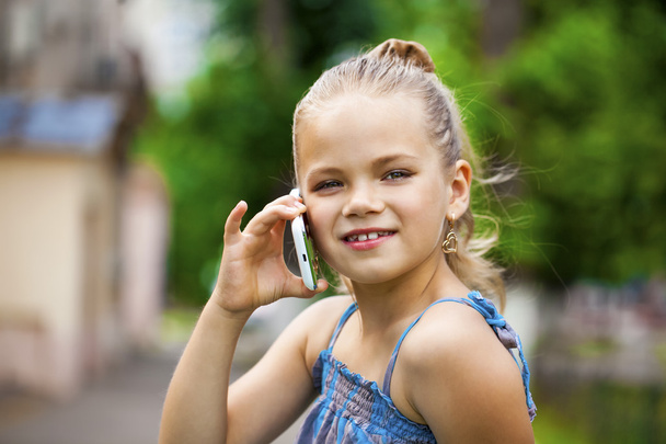 Little girl talking on cell phone against green of Park in summe - Фото, изображение