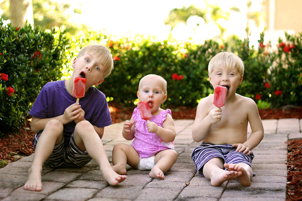 Tre bambini mangiano ghiaccioli di frutta all'aperto nella giornata estiva
 - Foto, immagini