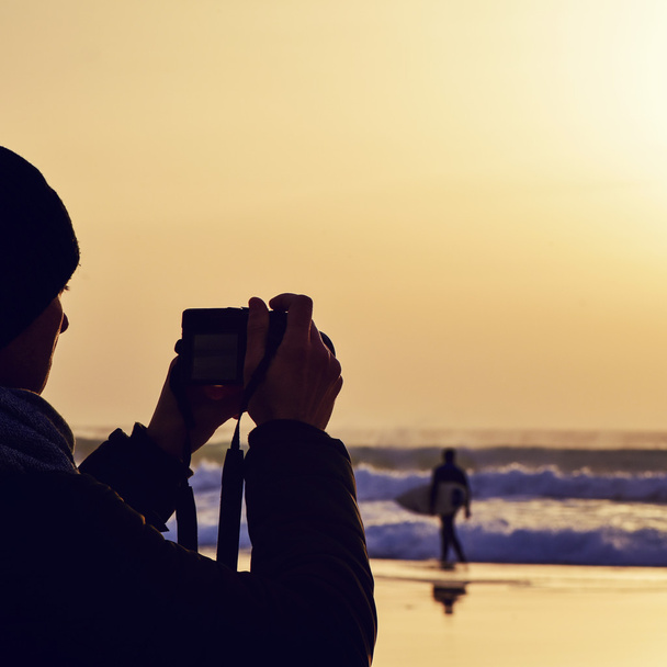 young man taking a picture in front of the sea at dusk - Фото, изображение
