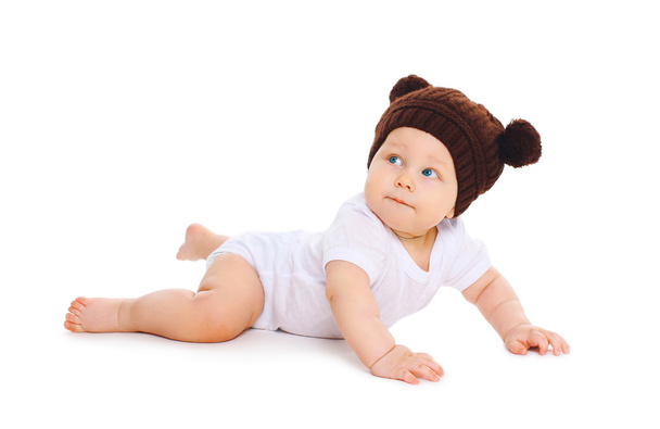 Cute baby in knitted brown hat with ears bears crawls on white b - Фото, зображення