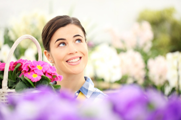 springtime woman smiling in garden and looking up with white wicker basket flowers of purple primroses - Photo, Image