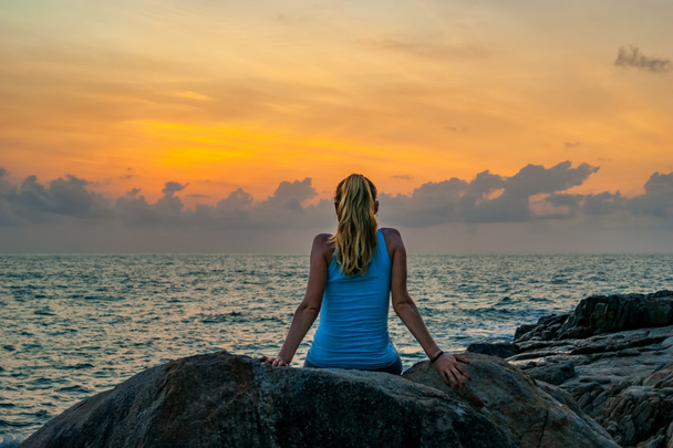 Jonge vrouw zittend op de rotsen van de zee en kijken naar de zonsopgang op een tropisch eiland - Foto, afbeelding