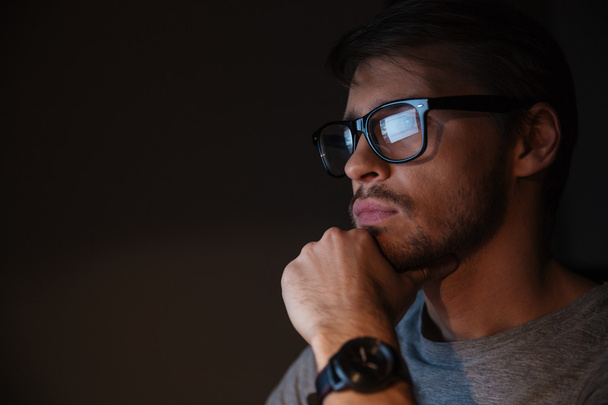 Крупный план сосредоточенного человека в очках, смотрящего на экран
 - Фото, изображение