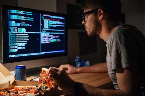 Concentrated software developer eating pizza and coding  - Valokuva, kuva