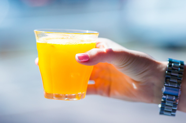 Χέρι που κρατά ποτήρι με φρέσκο χυμό πορτοκάλι στο υπαίθριο καφέ - Φωτογραφία, εικόνα