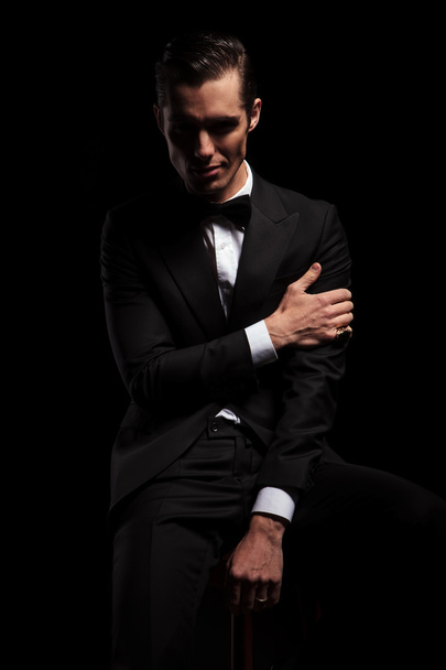 atractivo hombre en pose negra sentado tocando su brazo
 - Foto, imagen