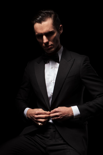 黒のスーツは暗いスタジオで座っているポーズの上品なビジネスマン  - 写真・画像