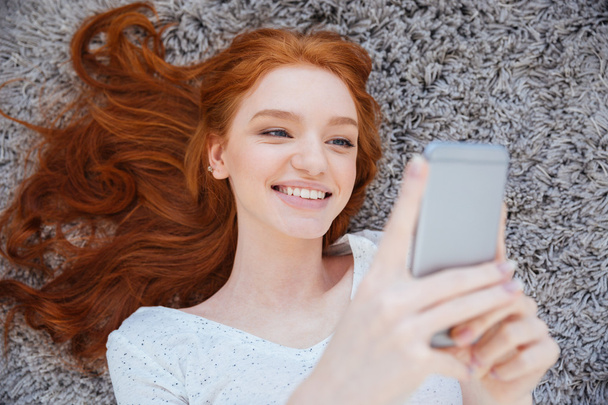 Woman lying on the carpet and using smartphone - Foto, Bild