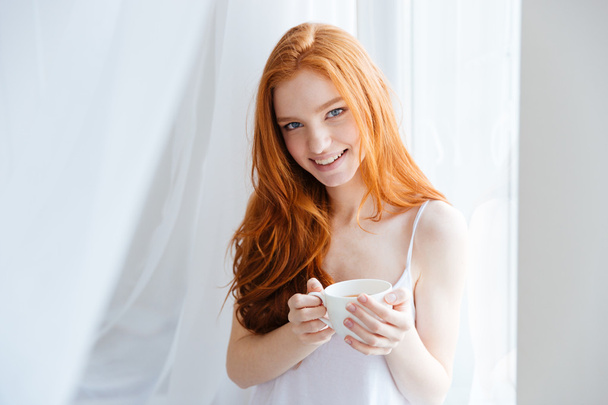 Redhead woman holding cup with tea at home - Foto, Bild