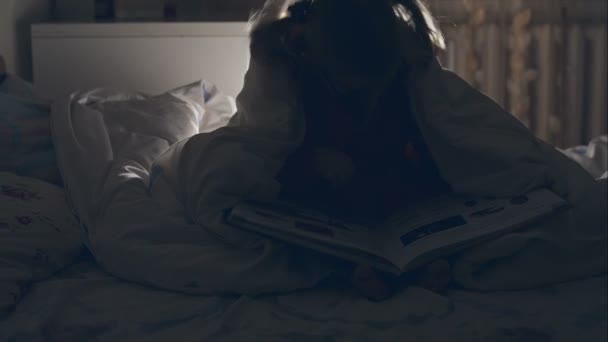 A young girl reading a book under the covers with a flashlight. RAW video record. - Video, Çekim
