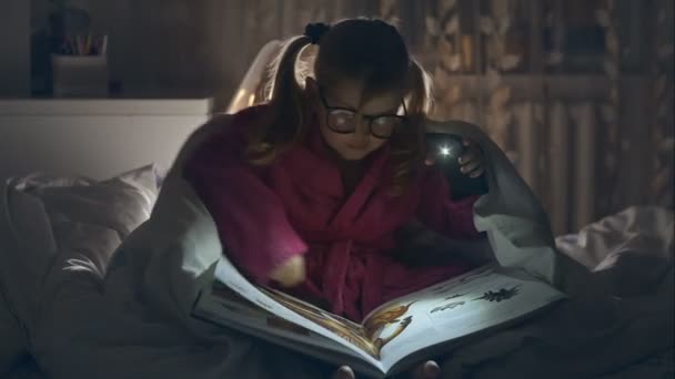 little girl sitting on the bed and reading a book - dolly motion. RAW video record. - Πλάνα, βίντεο
