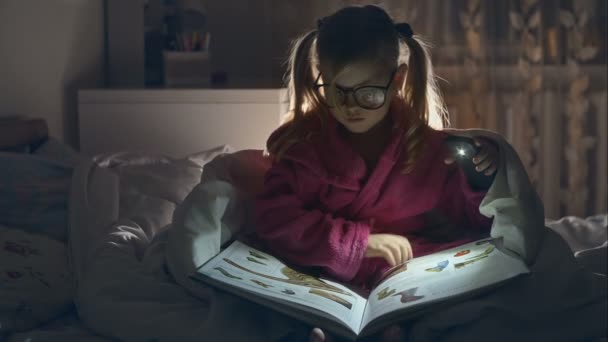The little girl with glasses reading a book sitting in bed under the covers. Big pleasure. RAW video record. - Video