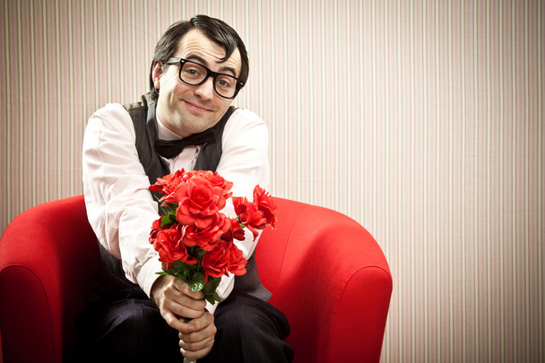 Nerd man wait his love on red armchair with flower gift - Fotografie, Obrázek