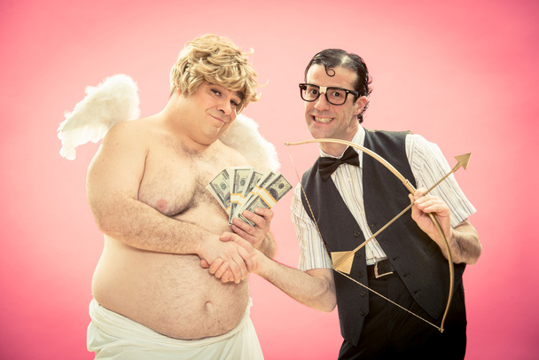 Nerd man with glasses buy with money love bow and arrow from cupid and give him handshake for valentine day - 写真・画像