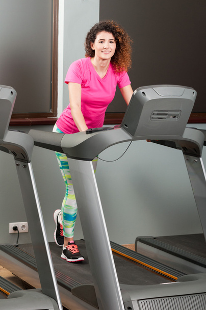 Attractive woman walking on running machine and smiling - Photo, Image